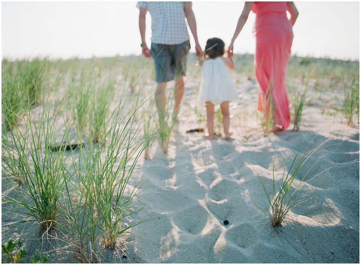 mom and dad walking with a little girl up the sandy path of Sandy Hook during a maternity session 