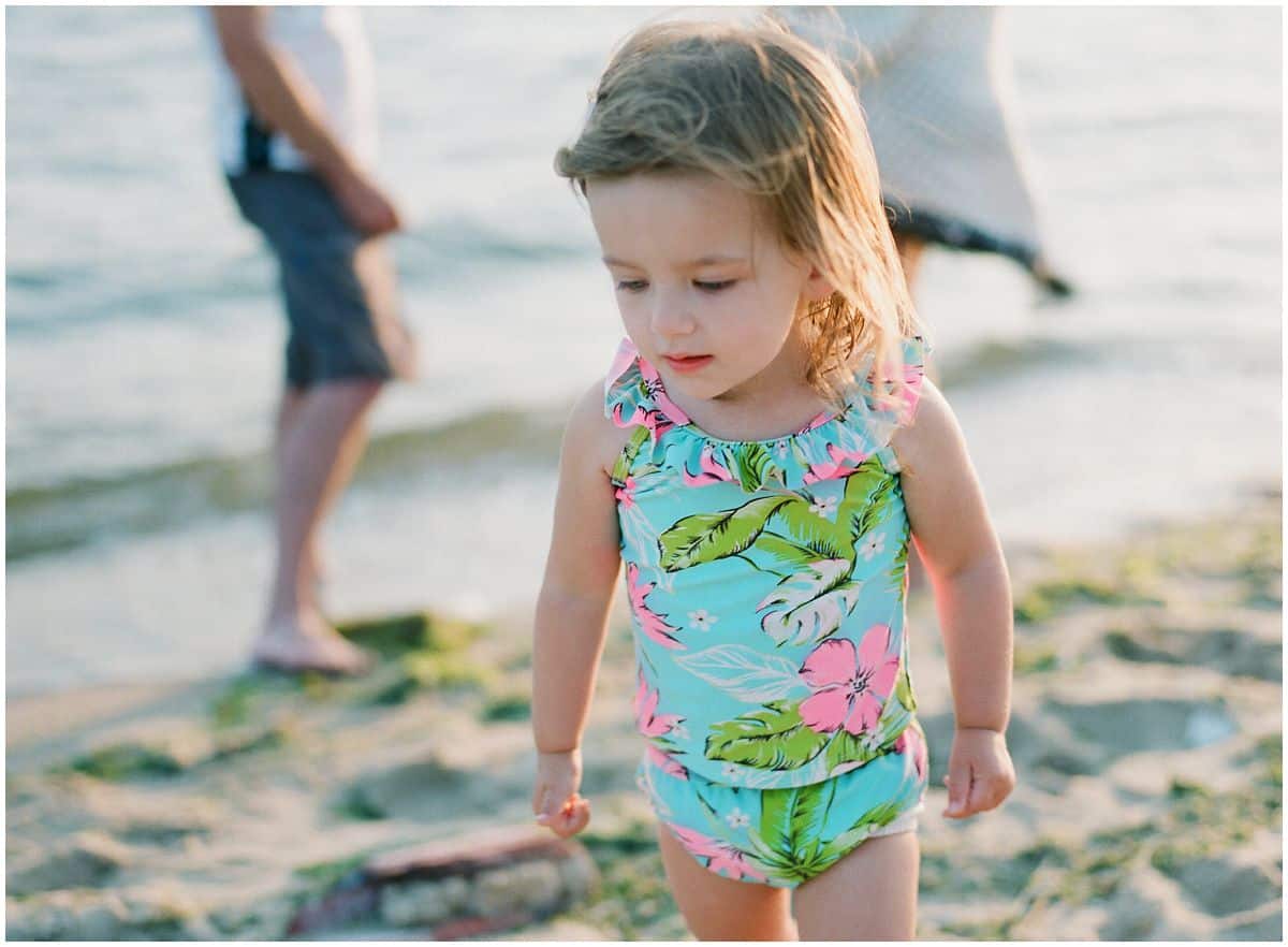 little girl in a turquoise and pink bathing suit walking on the sand by the beach waves of Sandy Hook NJ