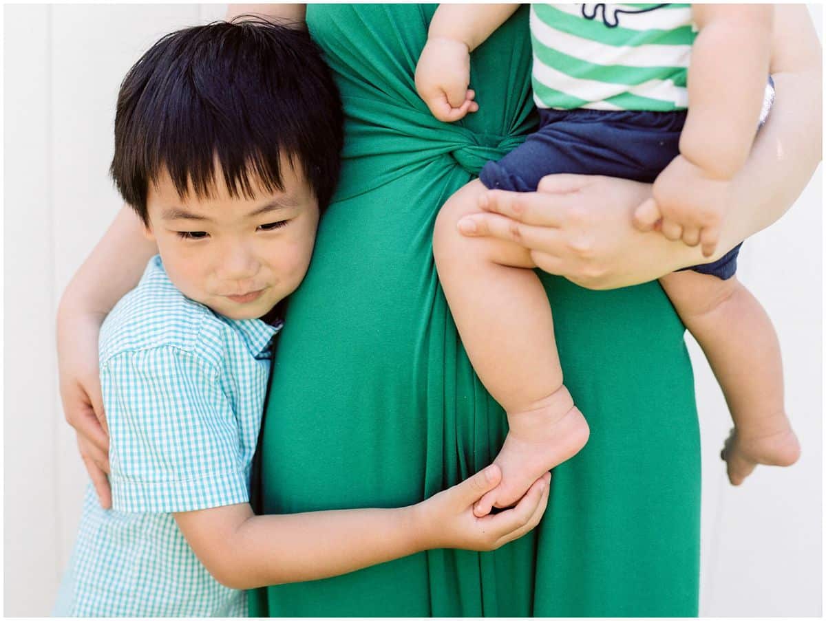 family portrait with mom in a green dress holding a baby and hugging her older son
