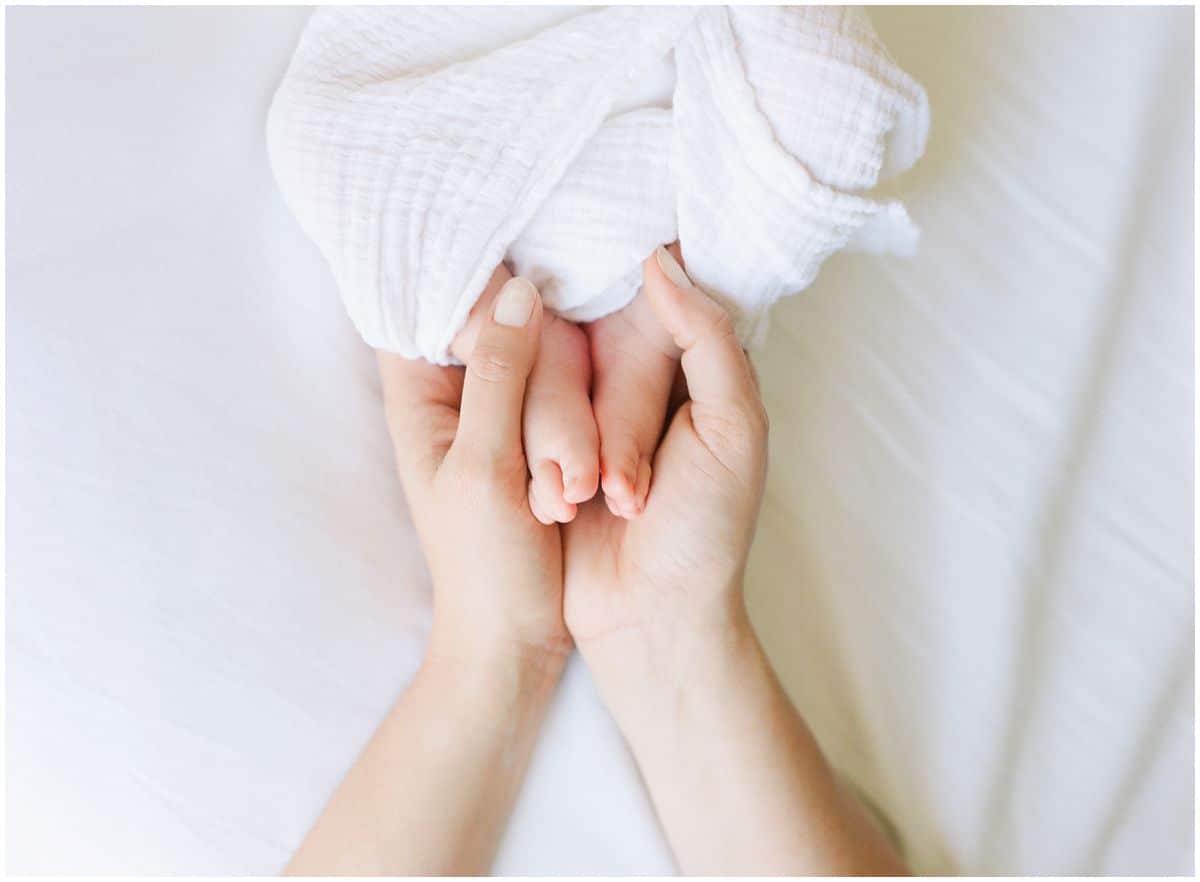 mom holding baby toes in her hands on a white bed
