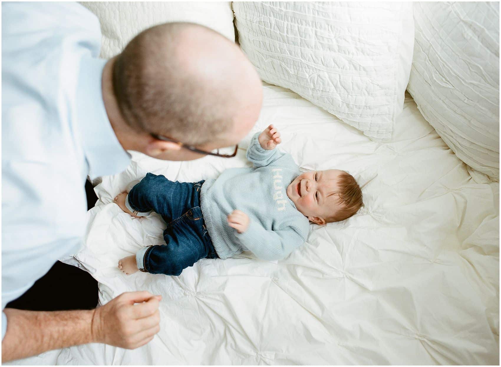 baby boy playing with his father on a bed