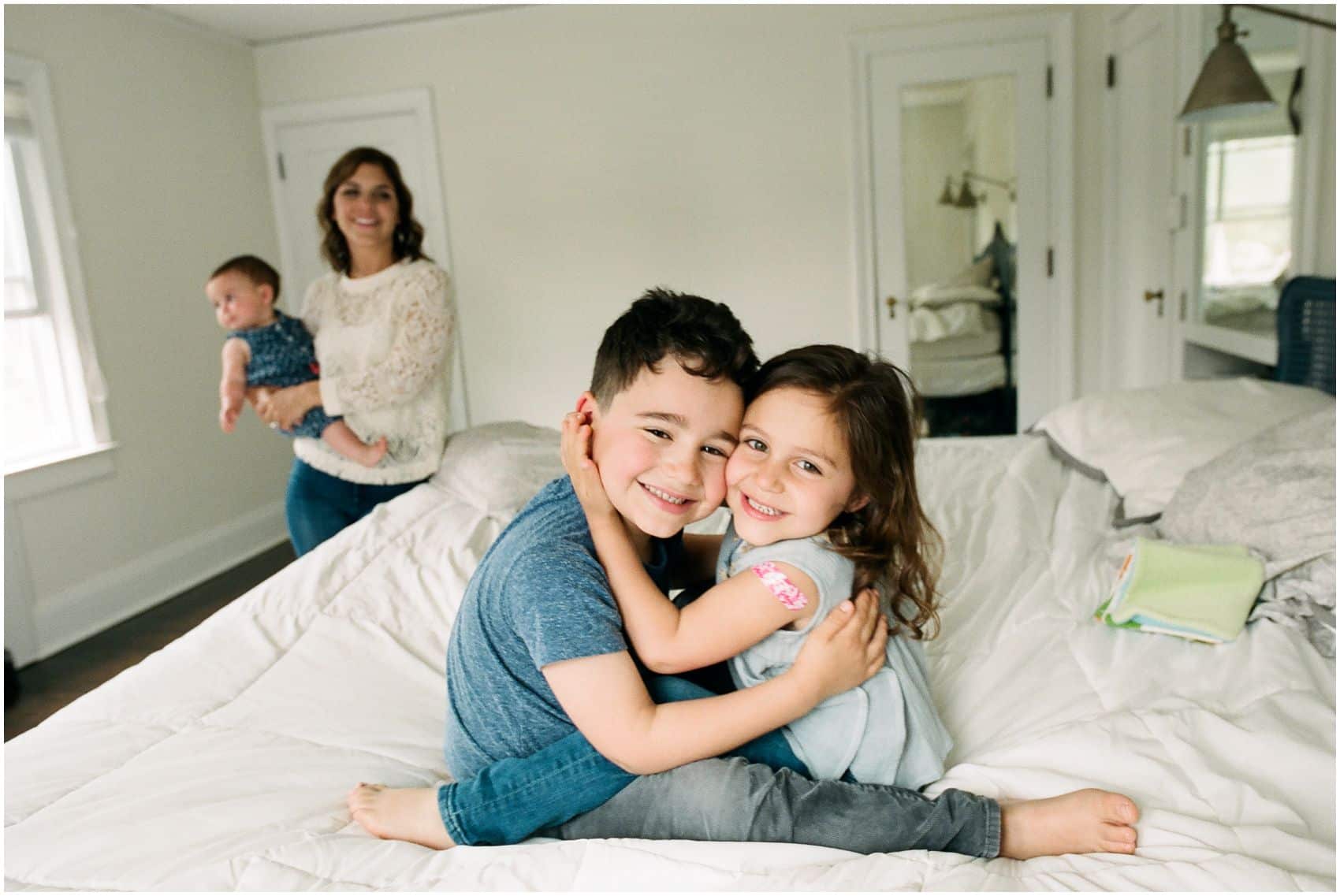 lifestyle family photography with brother and sister hugging each other on the bed of their Montclair NJ home