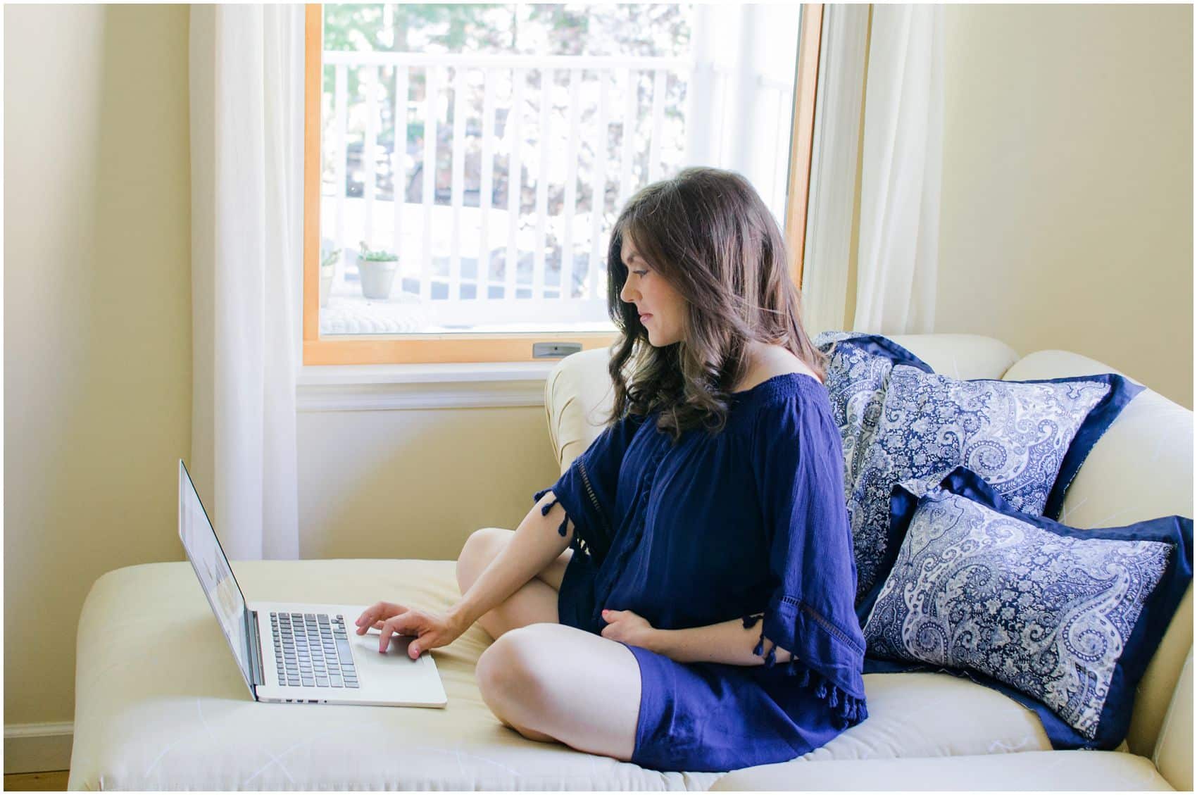 mom wearing royal blue maternity dress and working on apple computer in NYC home