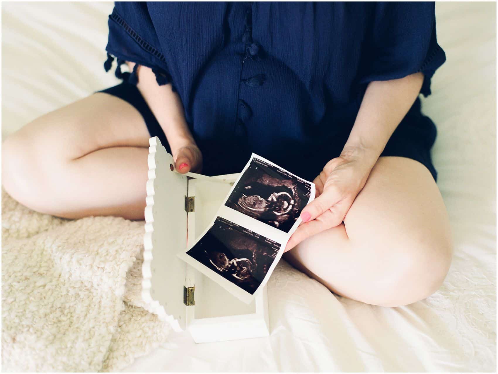 mom to be holding her baby's ultrasound photos and wearing a blue maternity dress