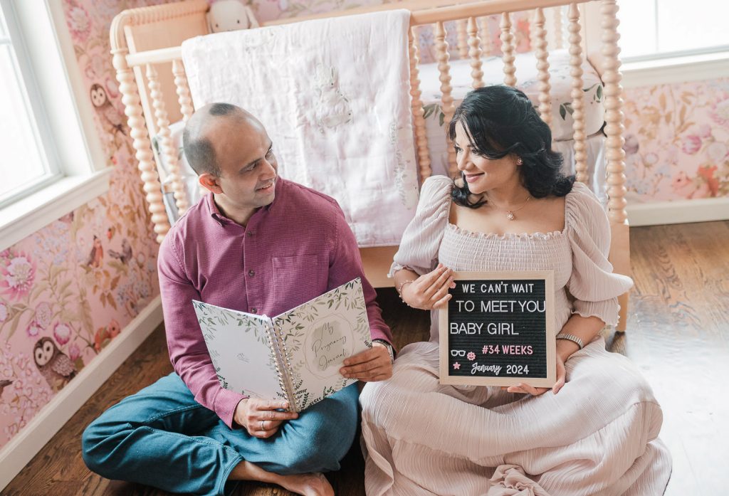 Couple holding pregnancy journal and letterboard sign reading we can't wait to meet you baby girl