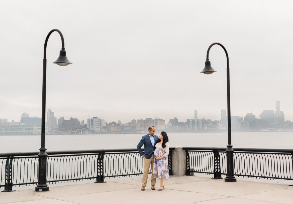 Couple holding baby announcement sign between two lampposts with Manhattan skyline