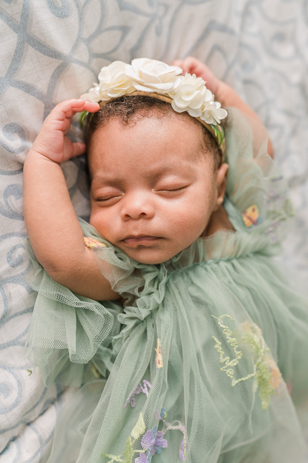 Sleeping newborn baby girl in sage green dress with floral headband — lifestyle newborn photographer NYC