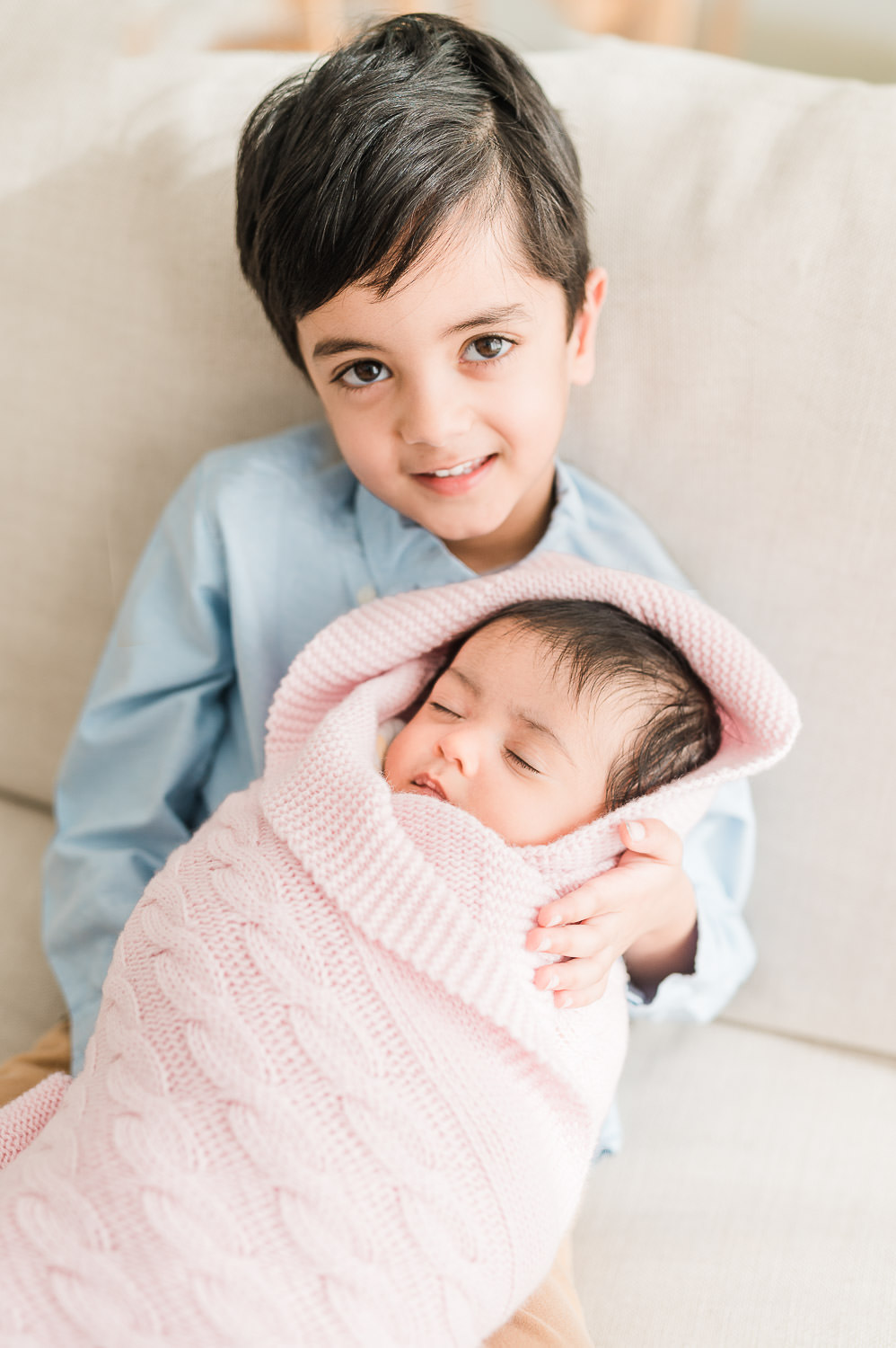 Older brother holding newborn baby sister swaddled in pink blanket — in-home newborn session NJ