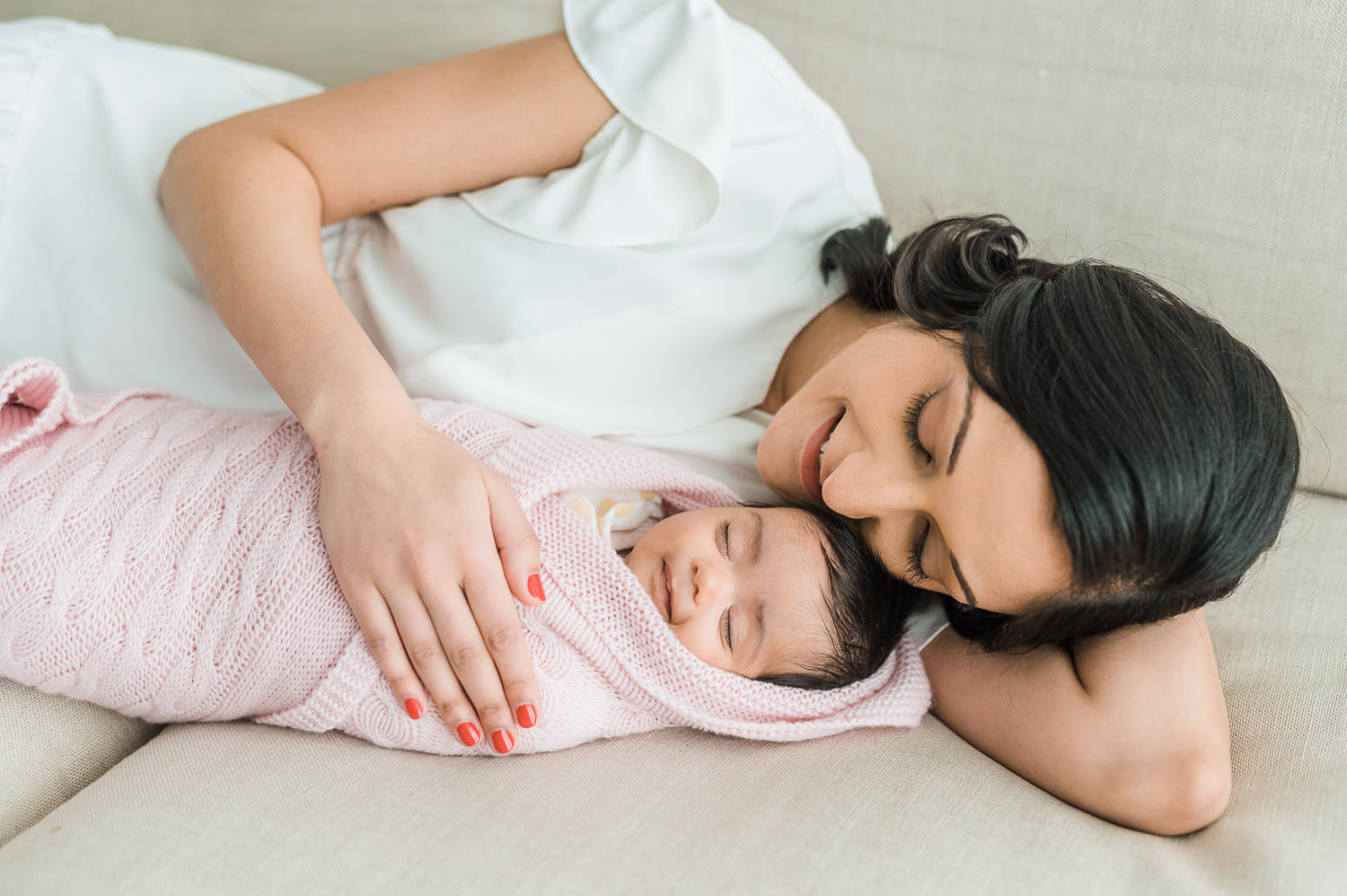 Mother lying next to newborn baby girl swaddled in pink blanket — in-home newborn photographer NYC