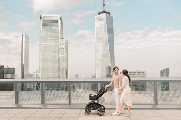 Newborn photography in New York City by Miriam Dubinsky, featuring a couple pushing a baby stroller near One World Trade Center, capturing timeless and natural moments