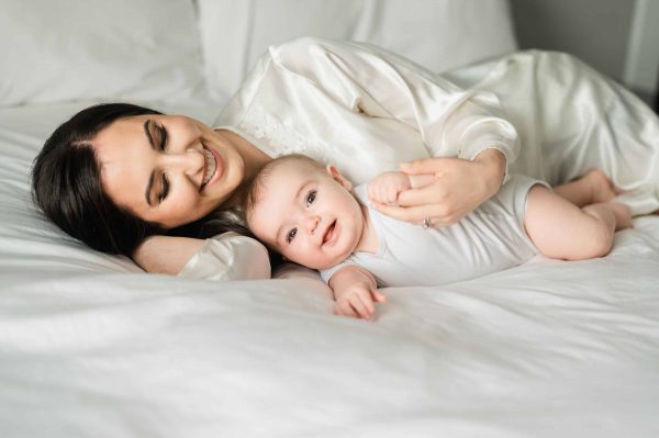 Timeless newborn photography in New York City, featuring a mother snuggling her smiling baby in a white silk robe
