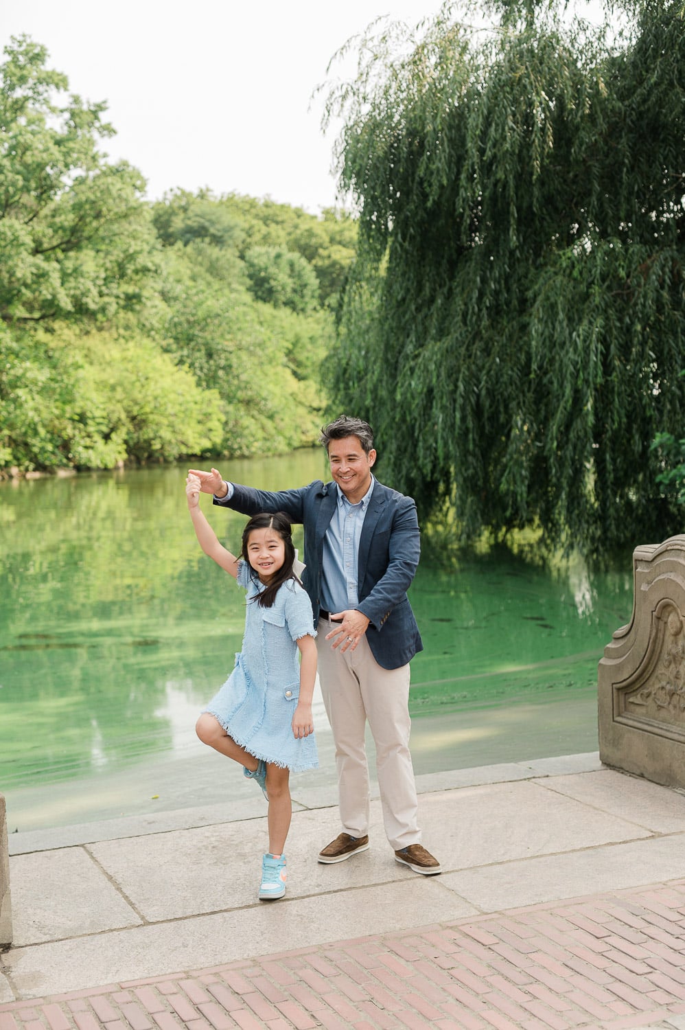 Father dancing with his daughter by the green water during Intimate family moment during Central Park family photography session NYC