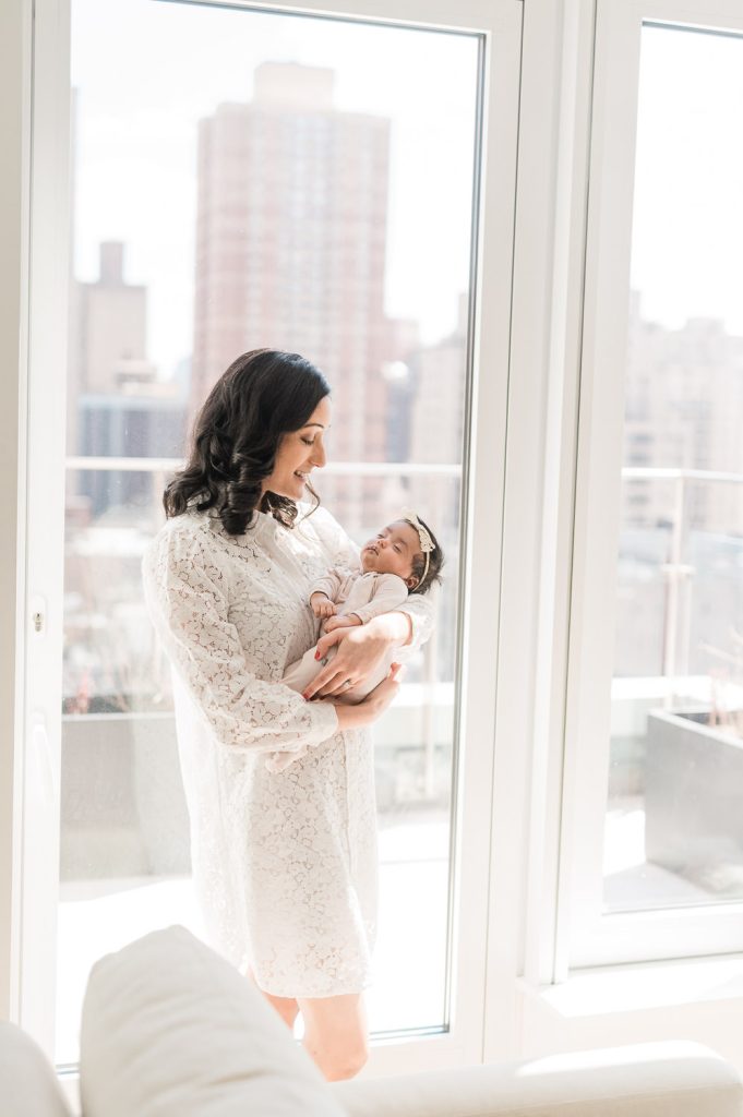 Mother holding newborn by window — in-home newborn photographer New York City