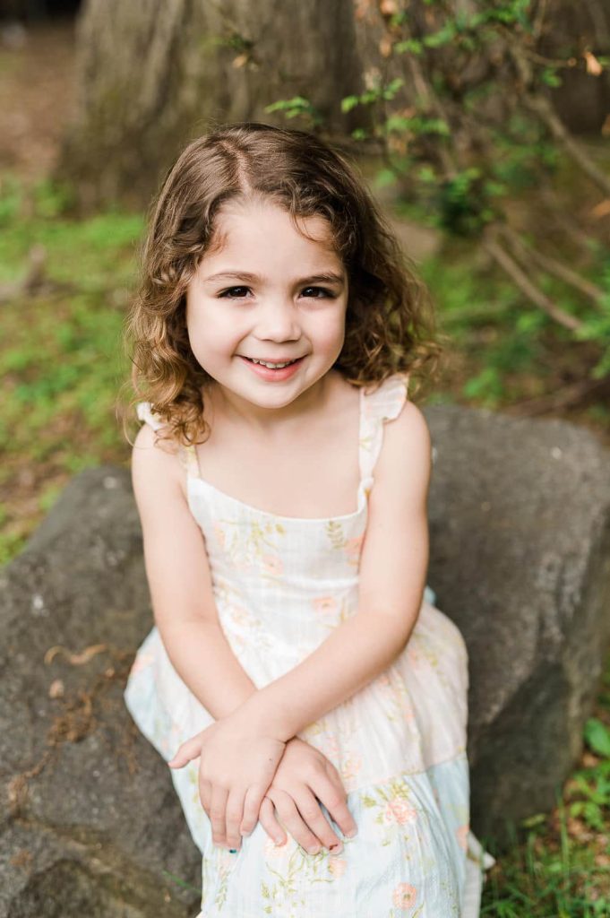 four year old girl sitting on rock during family photography session in Summit NJ