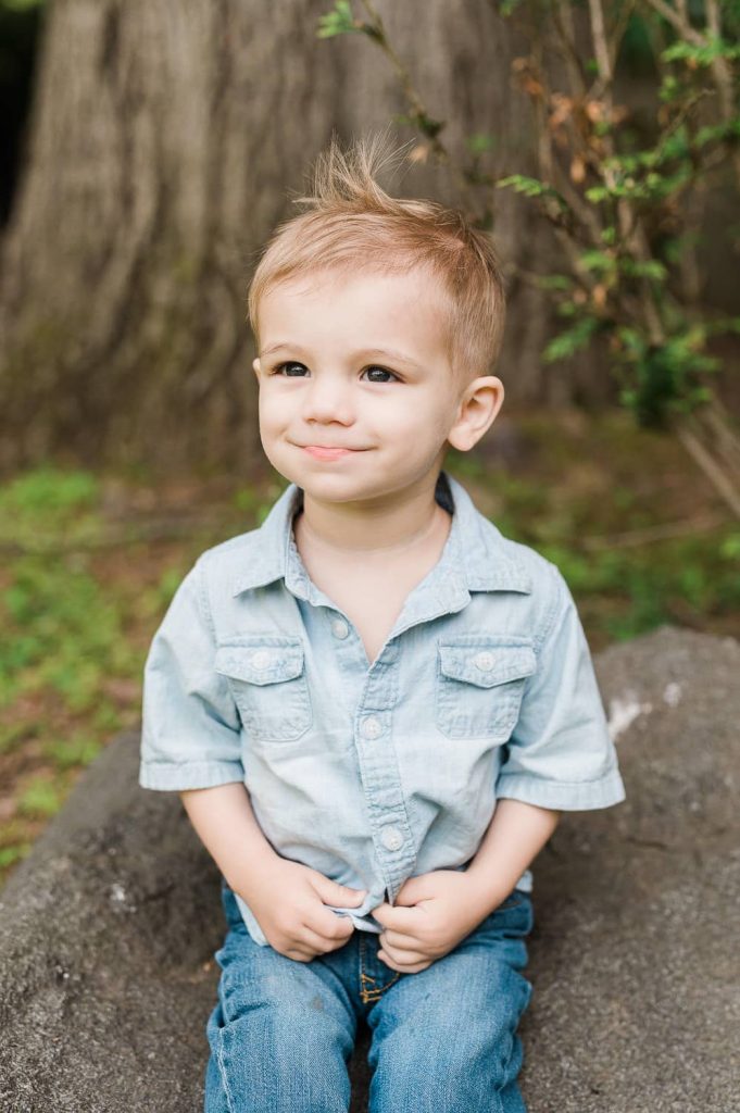 18 month old boy sitting on rock during lifestyle family photography session in Summit NJ