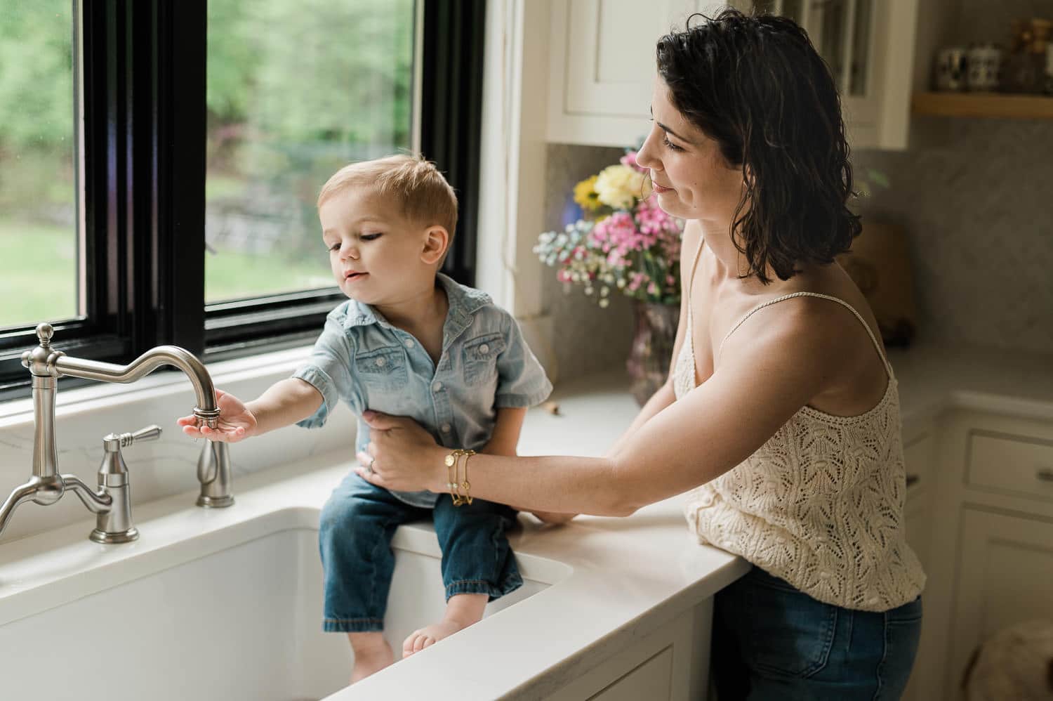 Mom and toddler playing with sink water by kitchen window in morning light, Summit, NJ family photography