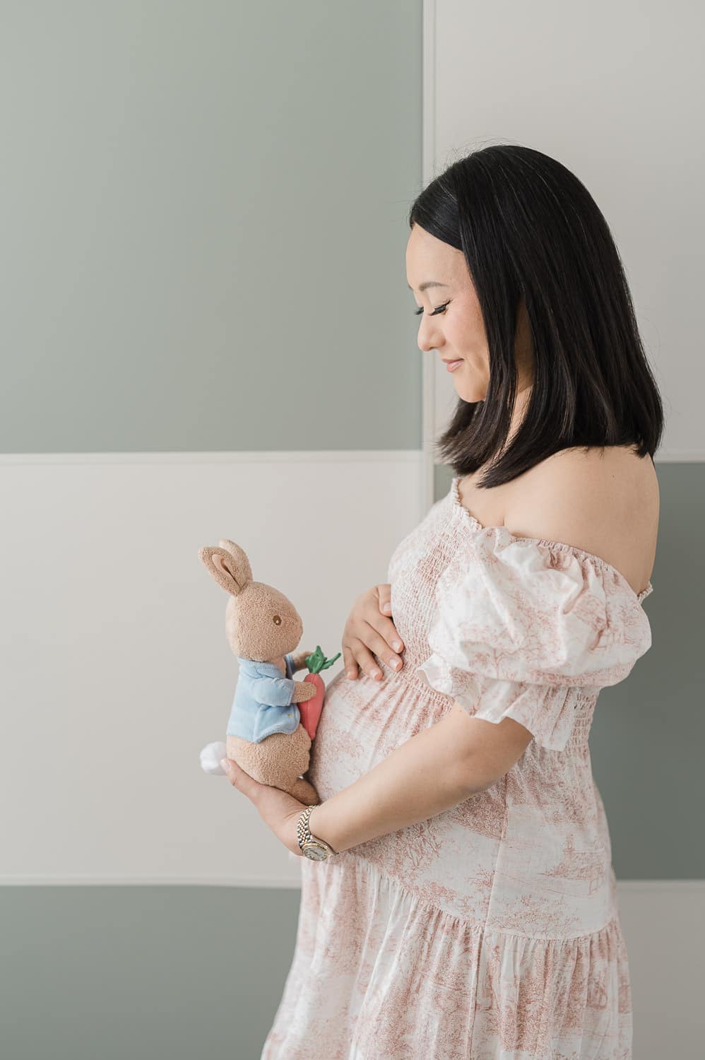 Expecting mother in nursery with a soft toy bunny on her belly during Brooklyn maternity session