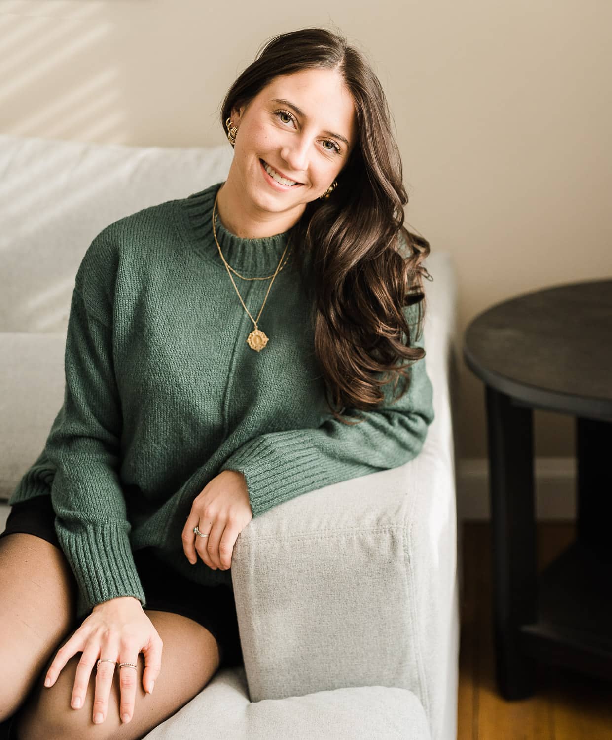Individual portrait of young woman seated on grey couch in Bergen County NJ for senior portraits by Miriam Dubinsky Photography 