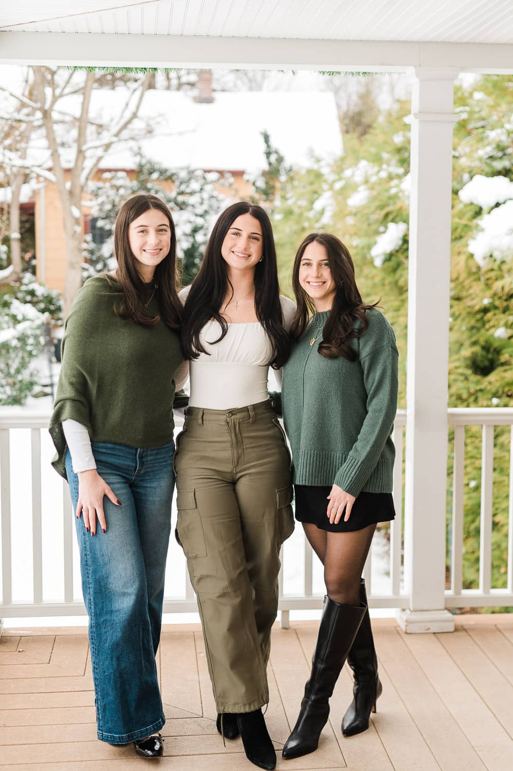 Three sisters standing together on snowy porch — family portrait session by Miriam Dubinsky Photography