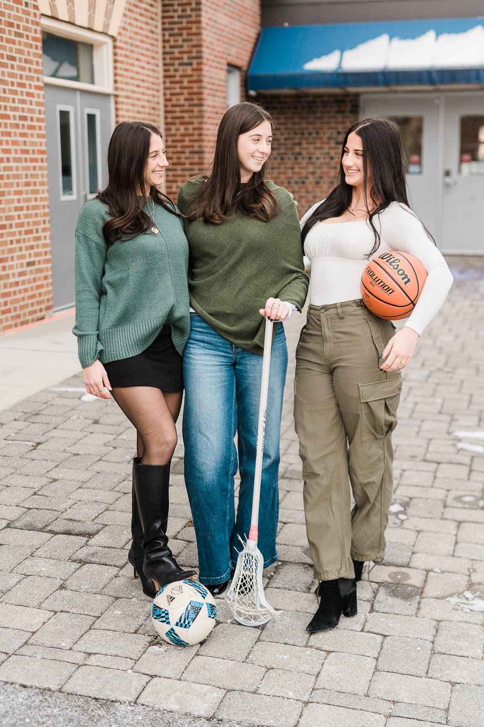 Three sisters holding basketball soccer ball and lacrosse stick in front of high school — Bergen County NJ senior portraits by Miriam Dubinsky Photography