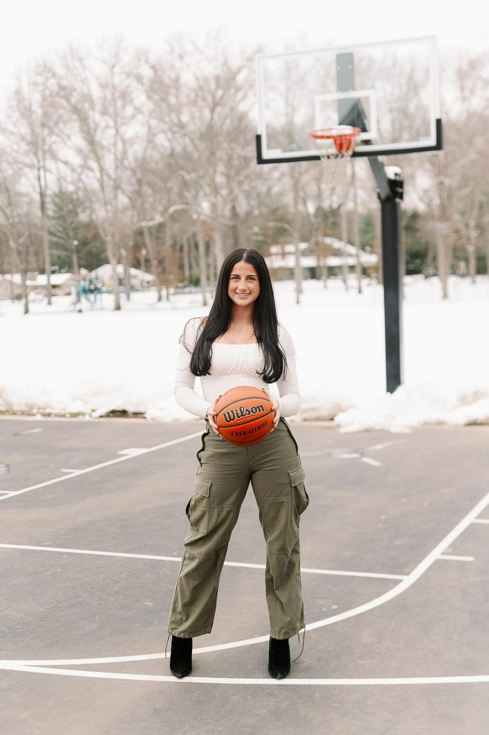 High school senior holding basketball on outdoor court in winter — senior portrait by Miriam Dubinsky Photography