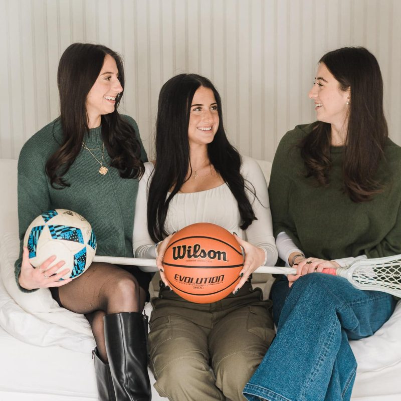 Three sisters laughing and holding soccer ball, basketball and lacrosse stick during senior portrait session in Bergen County NJ — senior portrait photographer Miriam Dubinsky