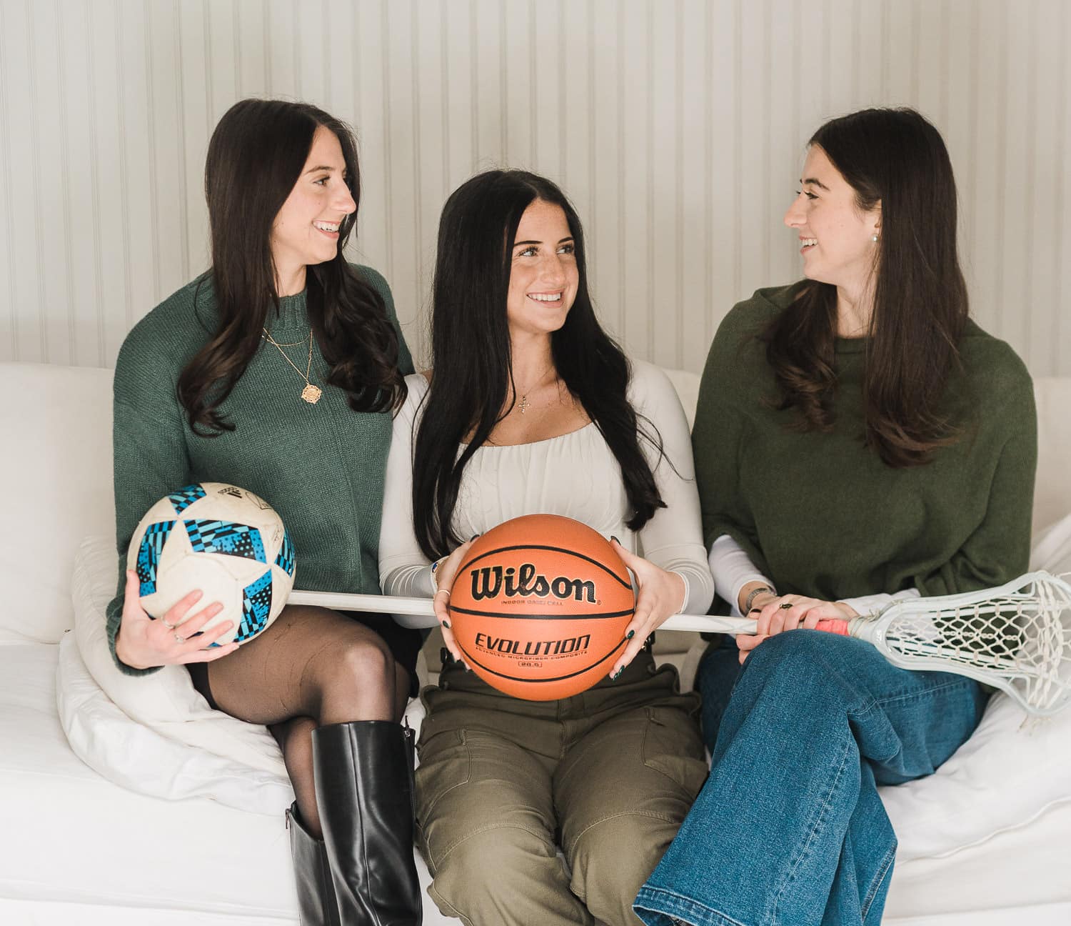 Three sisters laughing and holding soccer ball, basketball and lacrosse stick during senior portrait session in Bergen County NJ — senior portrait photographer Miriam Dubinsky