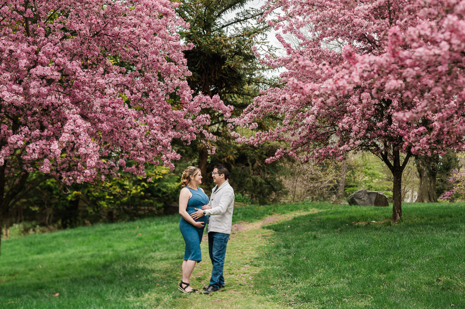 Cherry blossom maternity photos Morristown NJ — couple embracing under pink blossoms by Miriam Dubinsky Photography