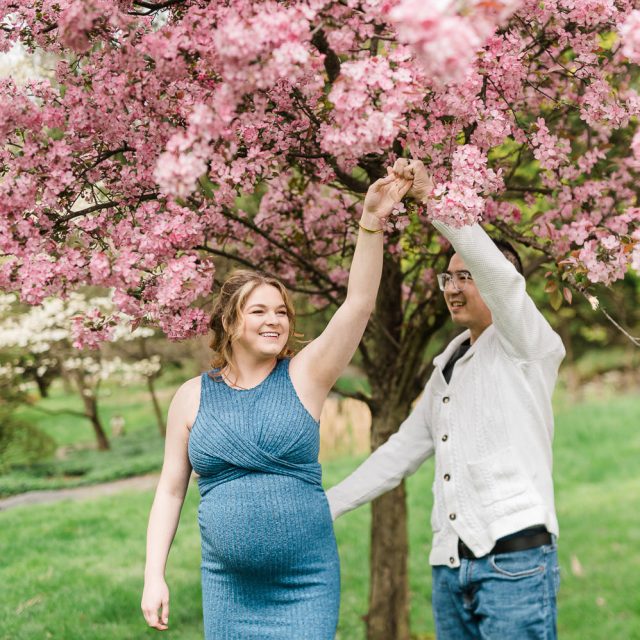 Cherry blossom maternity photos in NJ of couple dancing under pink blossoms in Morristown