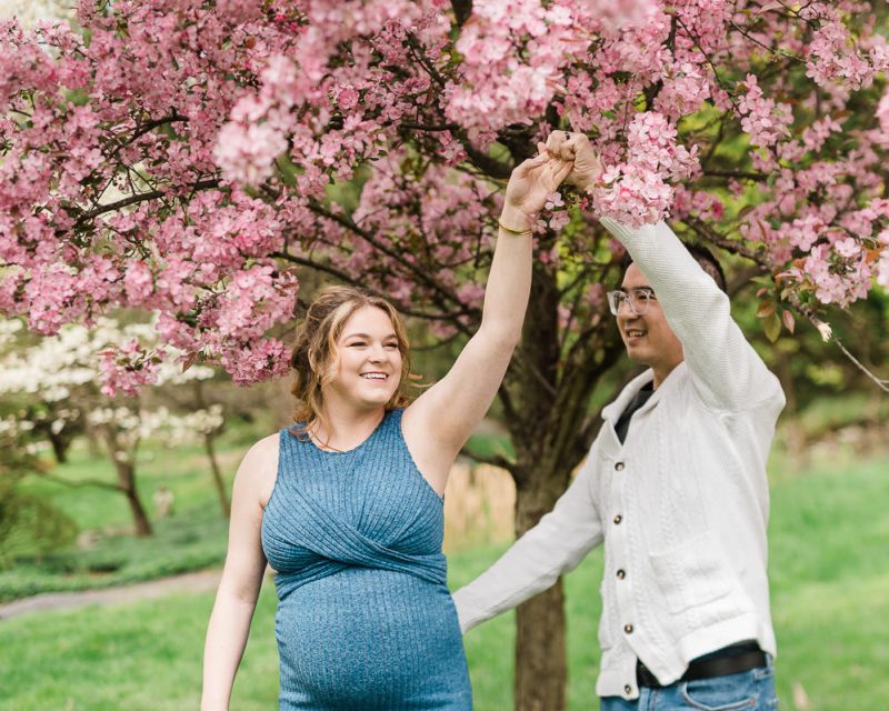 Cherry blossom maternity photos in NJ of couple dancing under pink blossoms in Morristown