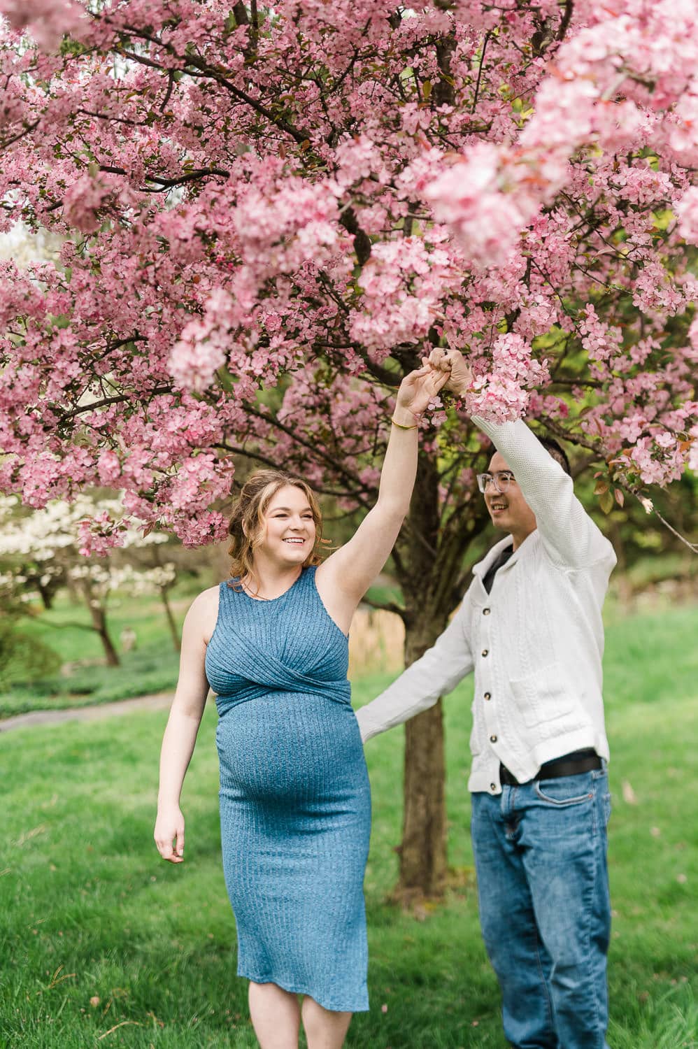 Cherry blossom maternity photos in NJ of couple dancing under pink blossoms in Morristown