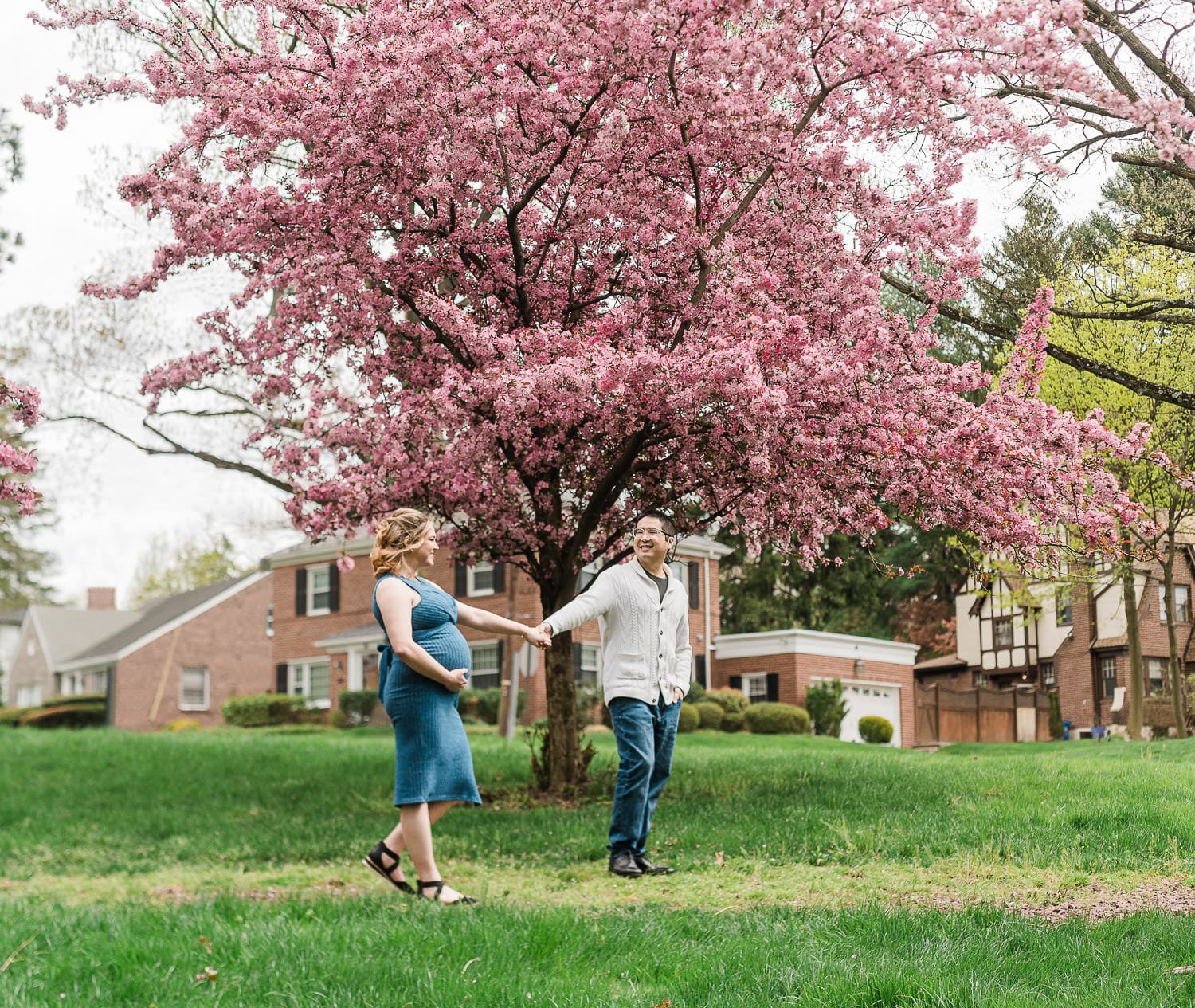 Cherry blossom maternity photos in NJ of couple walking under blooming trees in Morristown