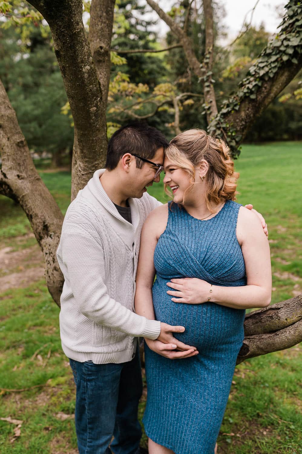 Couple laughing during cherry blossom maternity session in NJ under blooming trees