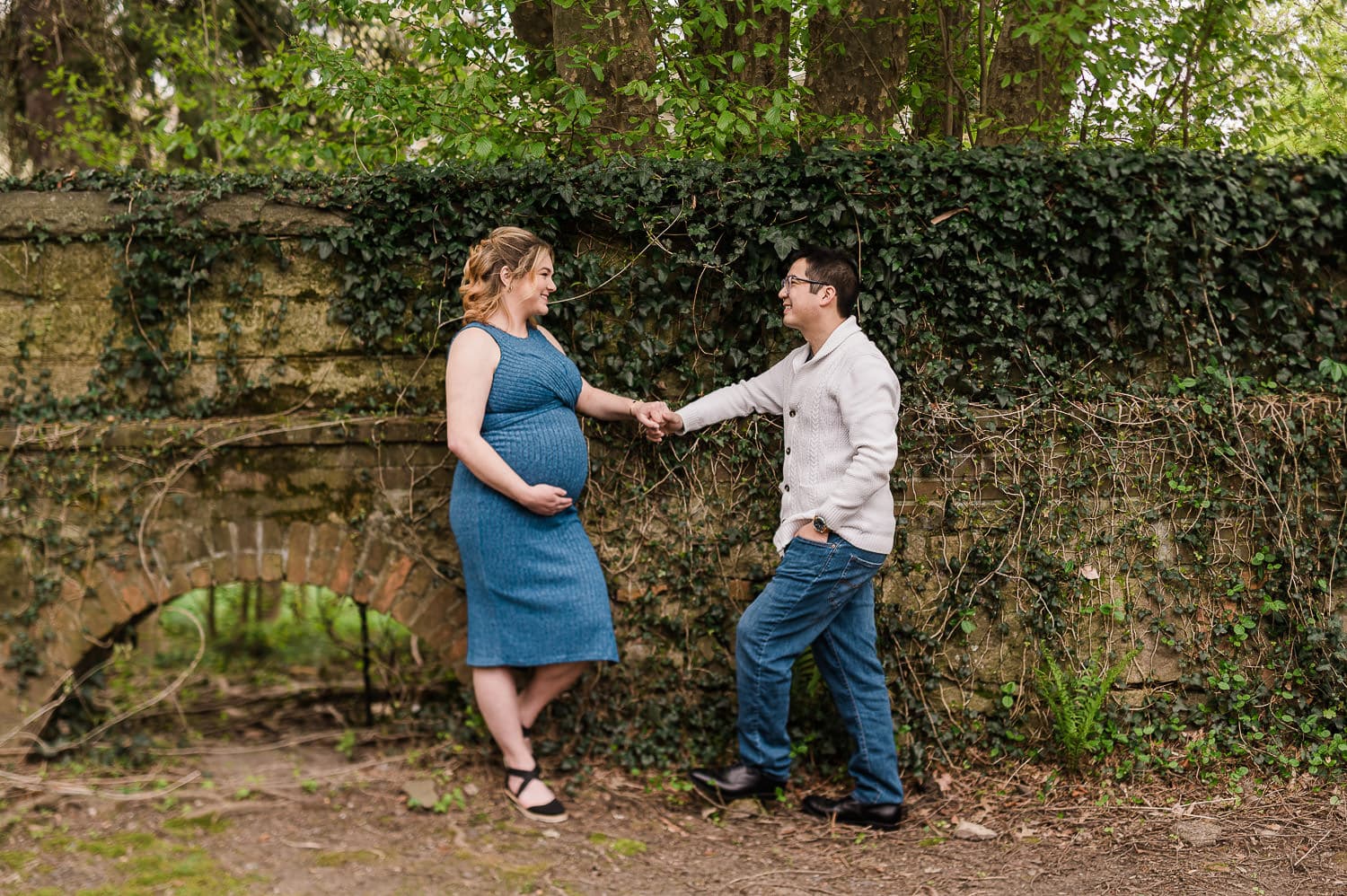 Expecting couple holding hands during outdoor maternity session in Morristown NJ near ivy-covered stone wall