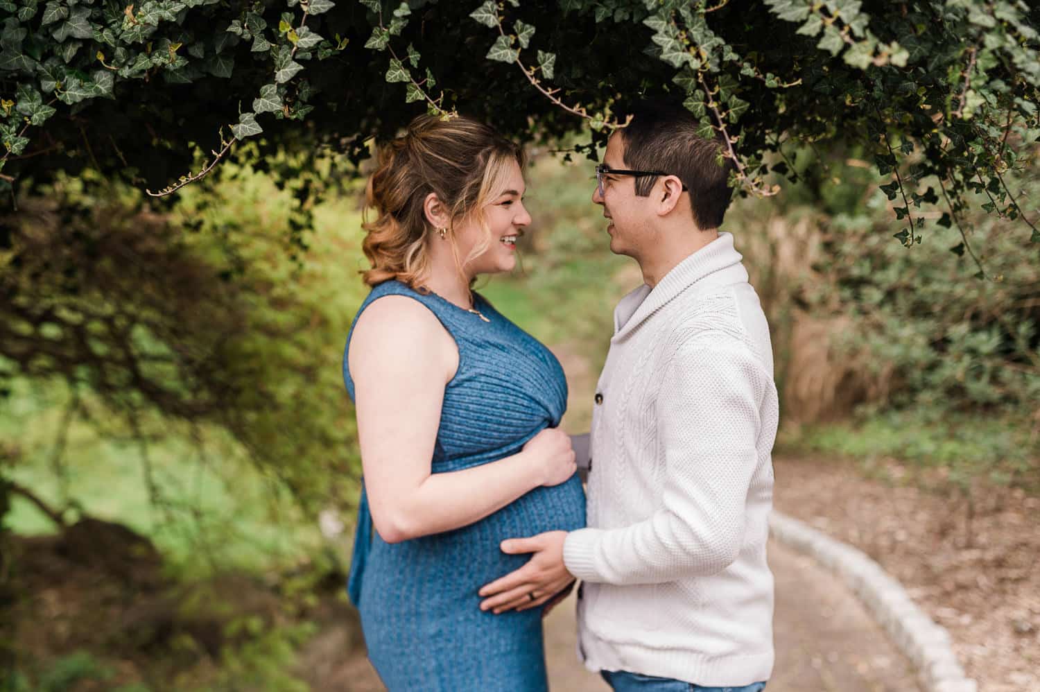 Couple holding baby bump during outdoor maternity session in Morristown NJ under greenery
