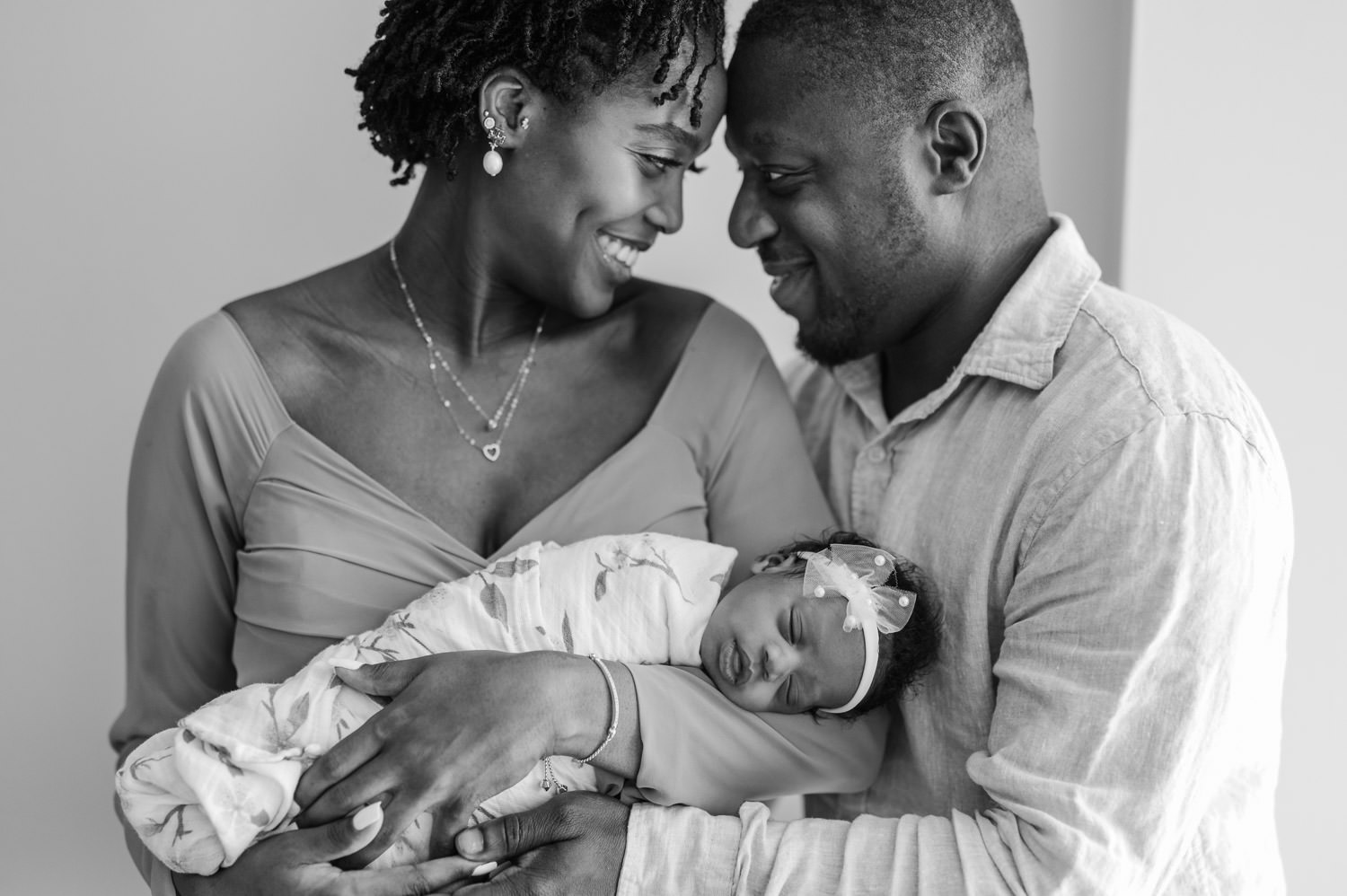 Parents smiling forehead to forehead with newborn baby girl  in black and white portrait
