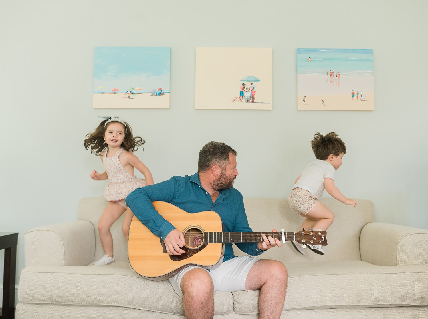 Dad playing acoustic guitar on sofa while older children dance around him — in-home newborn session Short Hills NJ