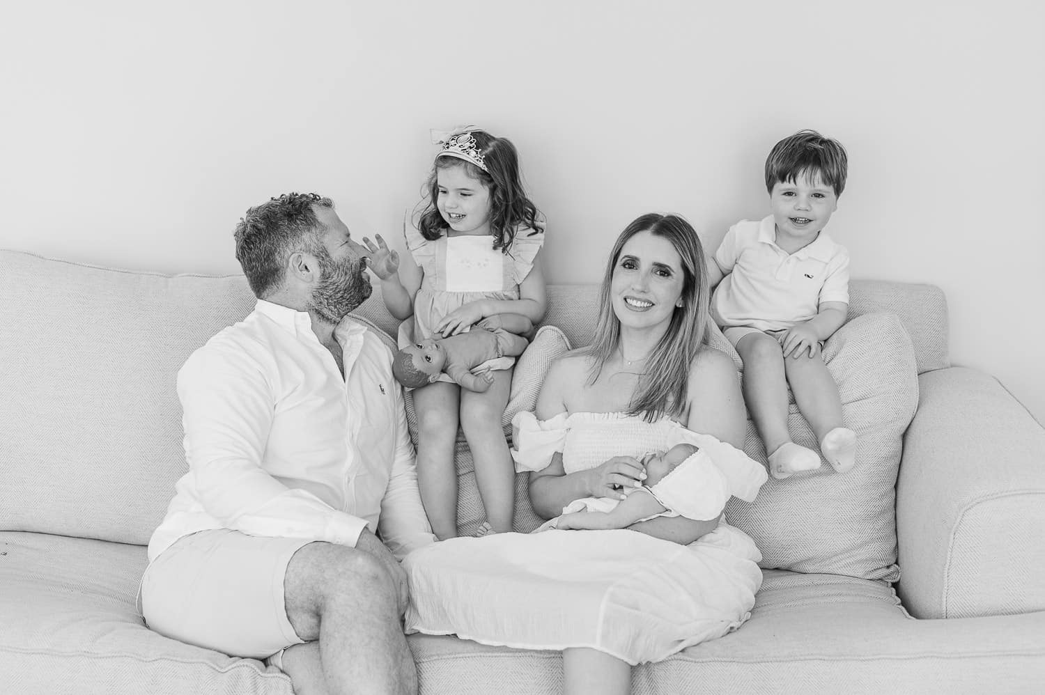 Family of five in white outfits on cream sofa with newborn baby — lifestyle newborn photographer Essex County NJ