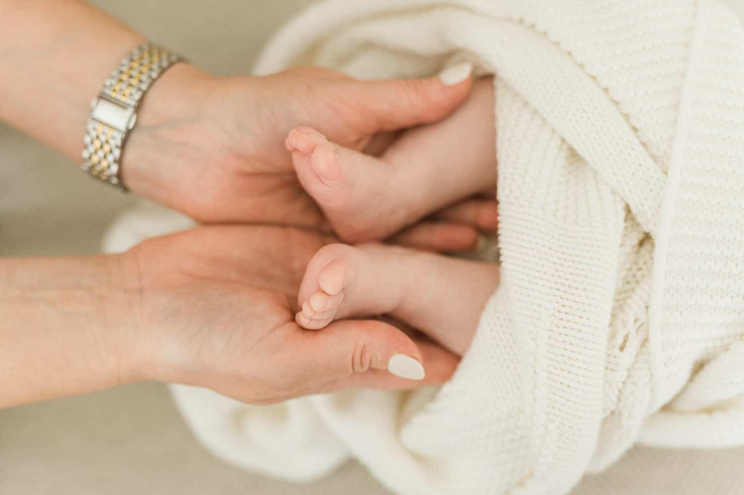 Close-up of mother's hands cradling newborn baby feet — in-home newborn photographer Miriam Dubinsky