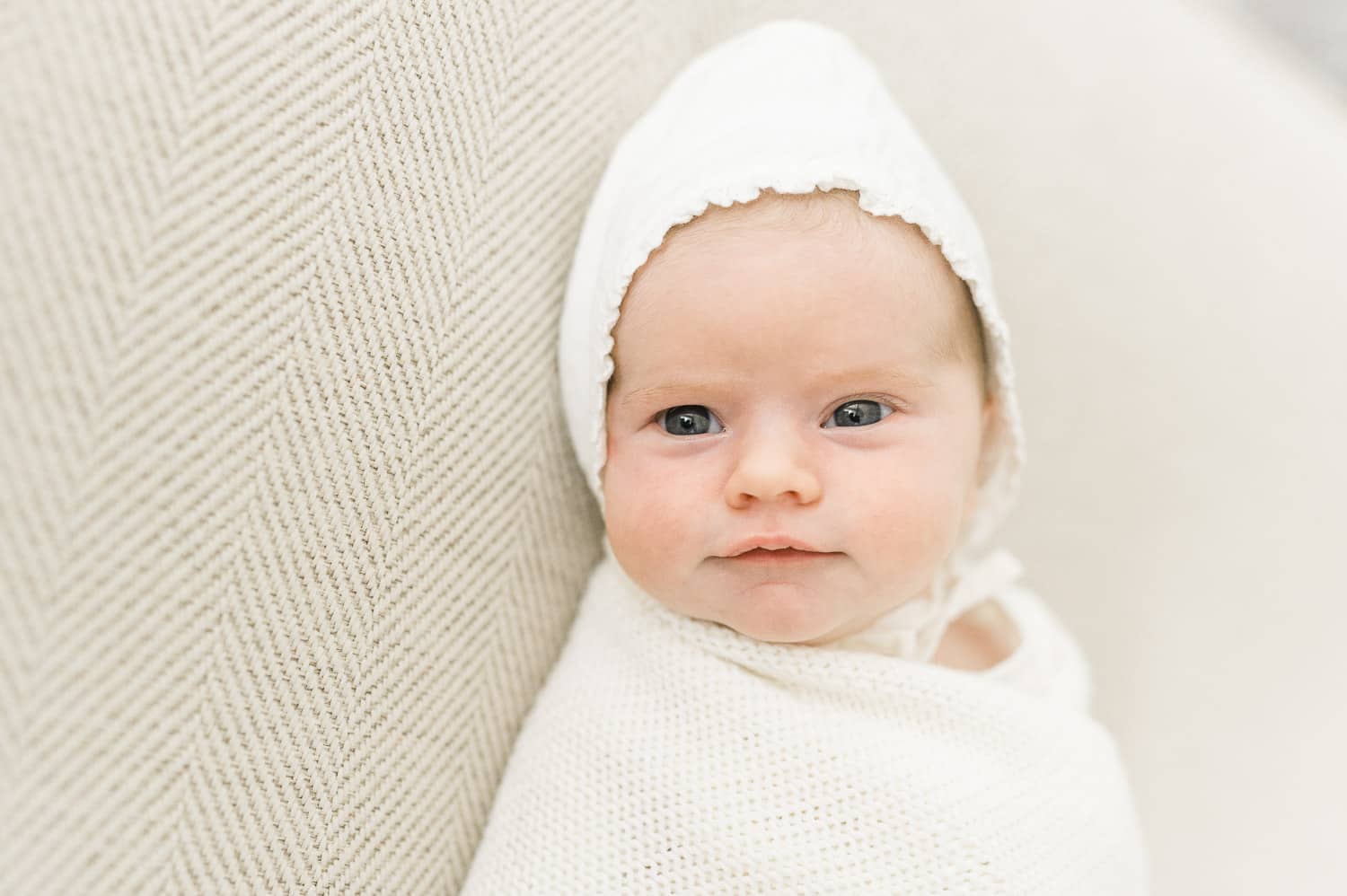 Newborn baby girl wearing white bonnet and wrapped in cream knit blanket