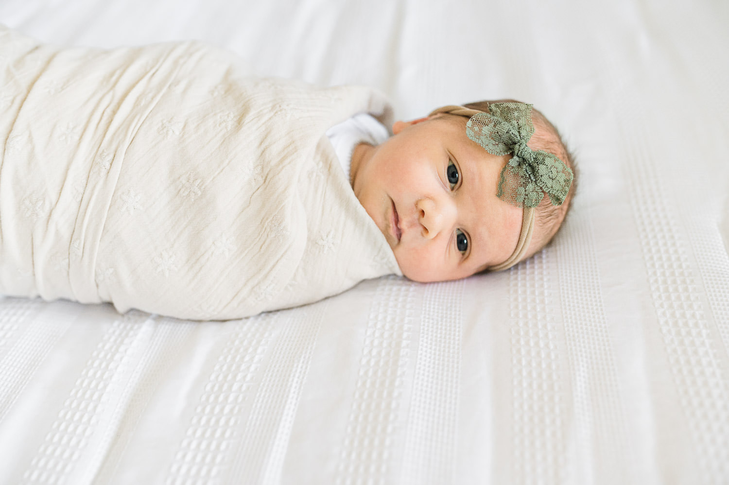 Baby sister awake wearing a green bow  for her  newborn photos with Miriam Dubinsky Photography