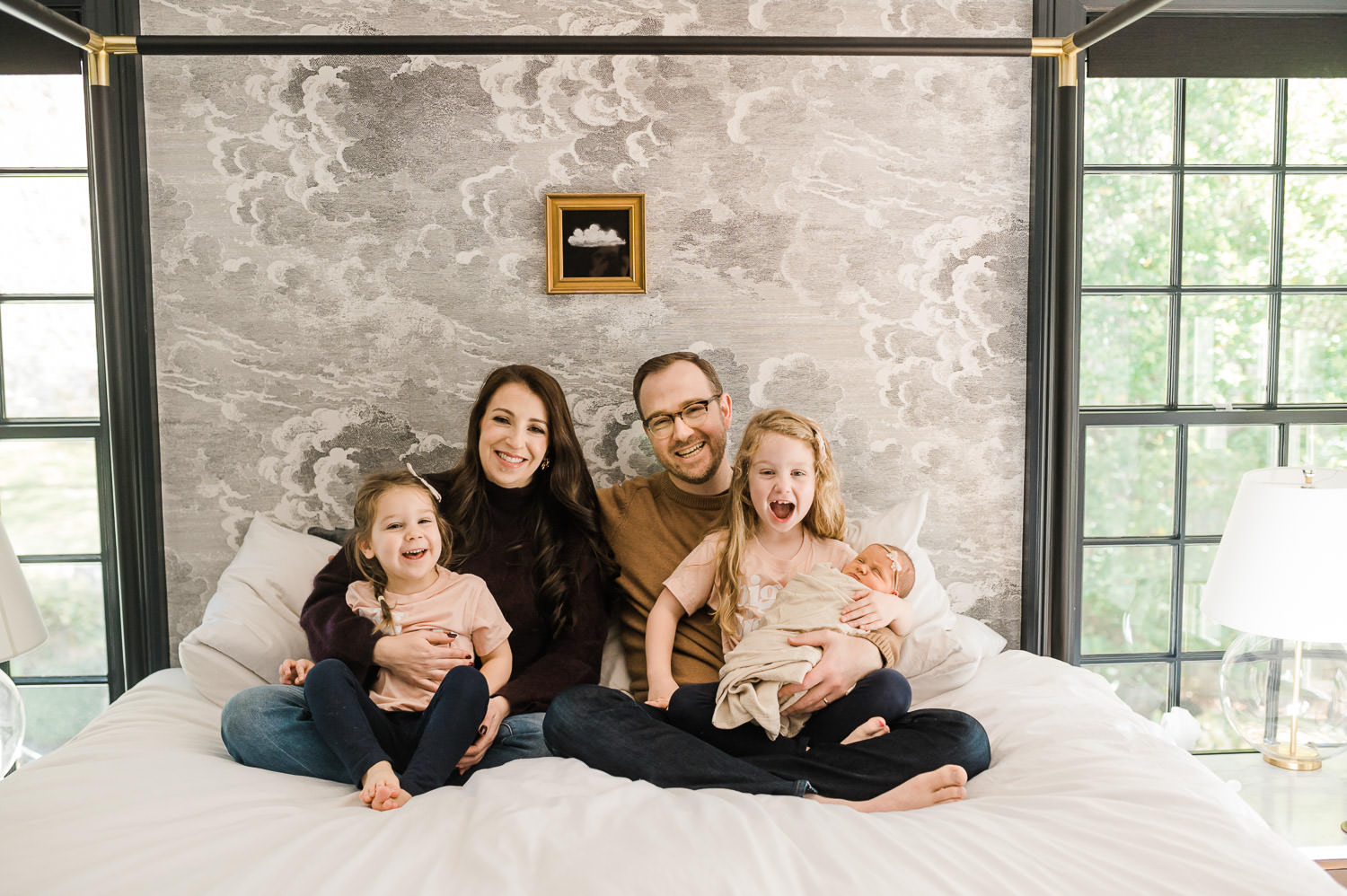 happy mom and dad hugging their tree kids including baby girl in their bedroom during NYC newborn photography session
