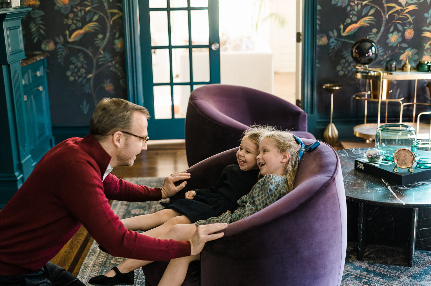 father is laughing with his two small daughters in their living room armchair