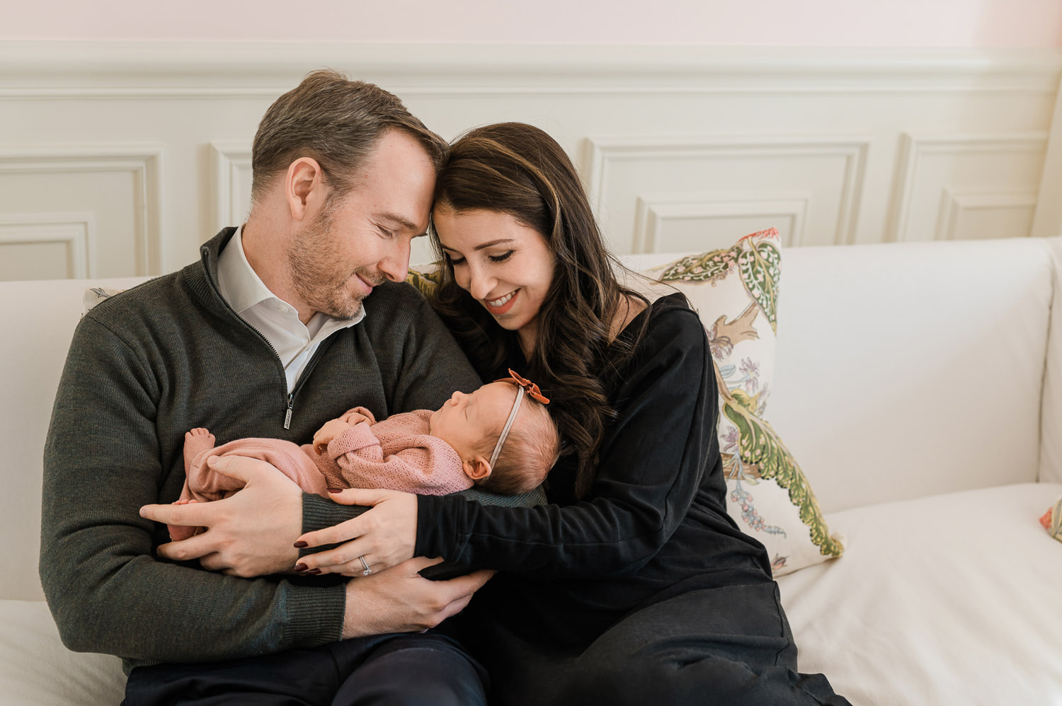 new parents embracing their new baby girl with a bow sitting on the couch in their Manhattan home
